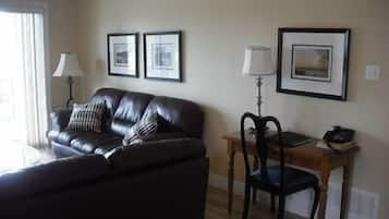Een woonkamer met een zwarte leren bank, een houten bijzettafeltje en een stoel. Er hangen drie ingekaderde foto's aan de muur.