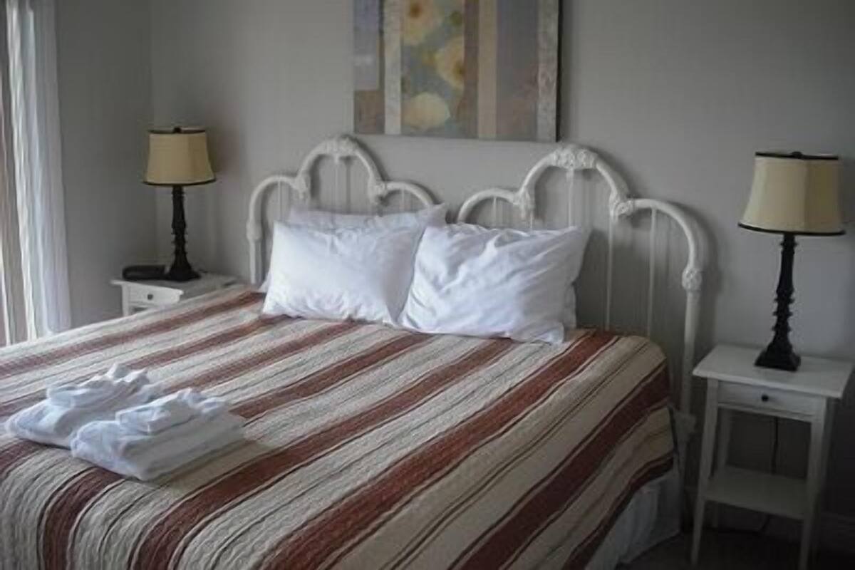A bed with a striped bedspread, two white pillows, and a folded towel. There are two bedside tables with lamps.