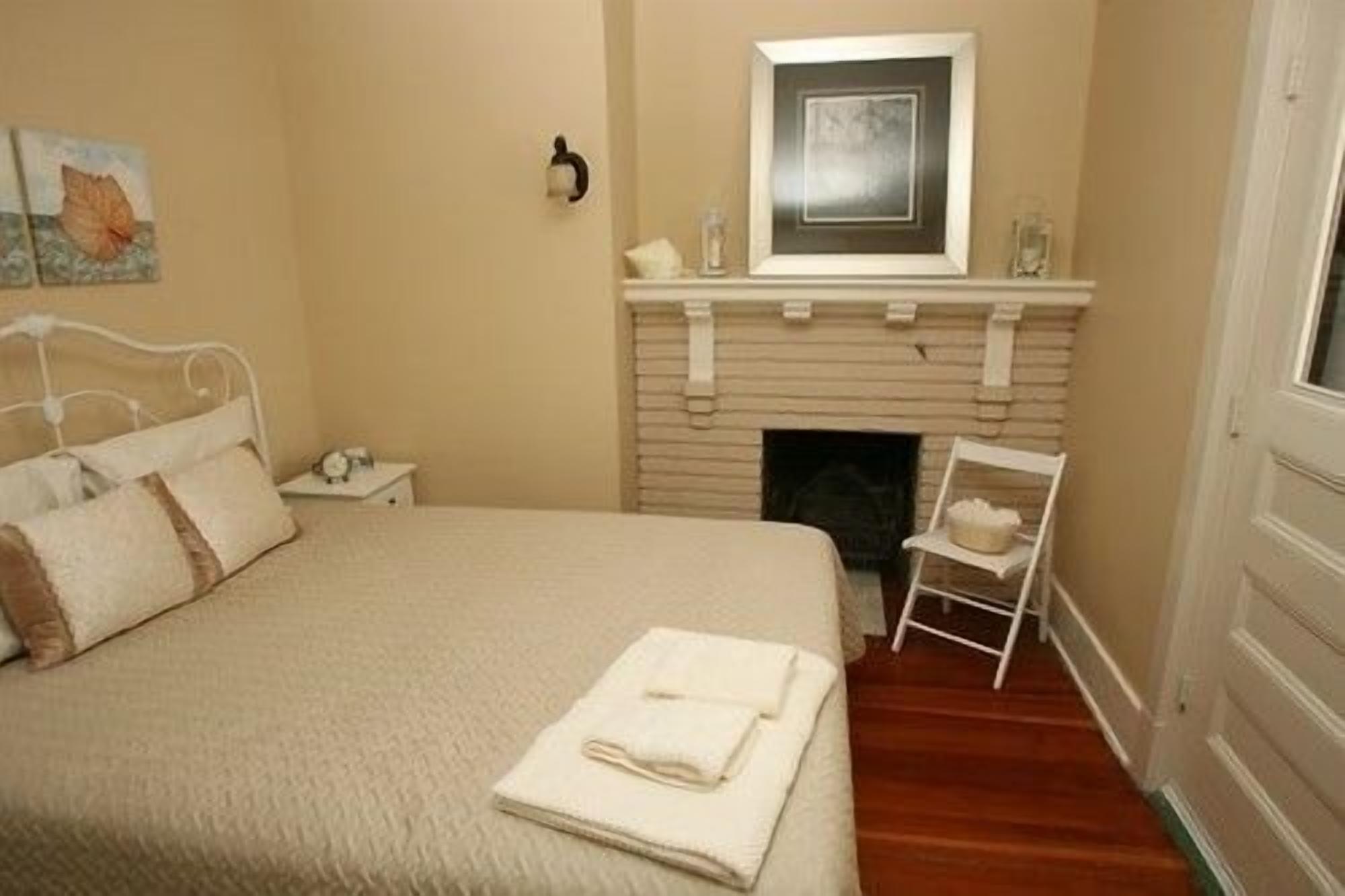 Een slaapkamer met een bed, een open haard, een nachtkastje en een stoel.