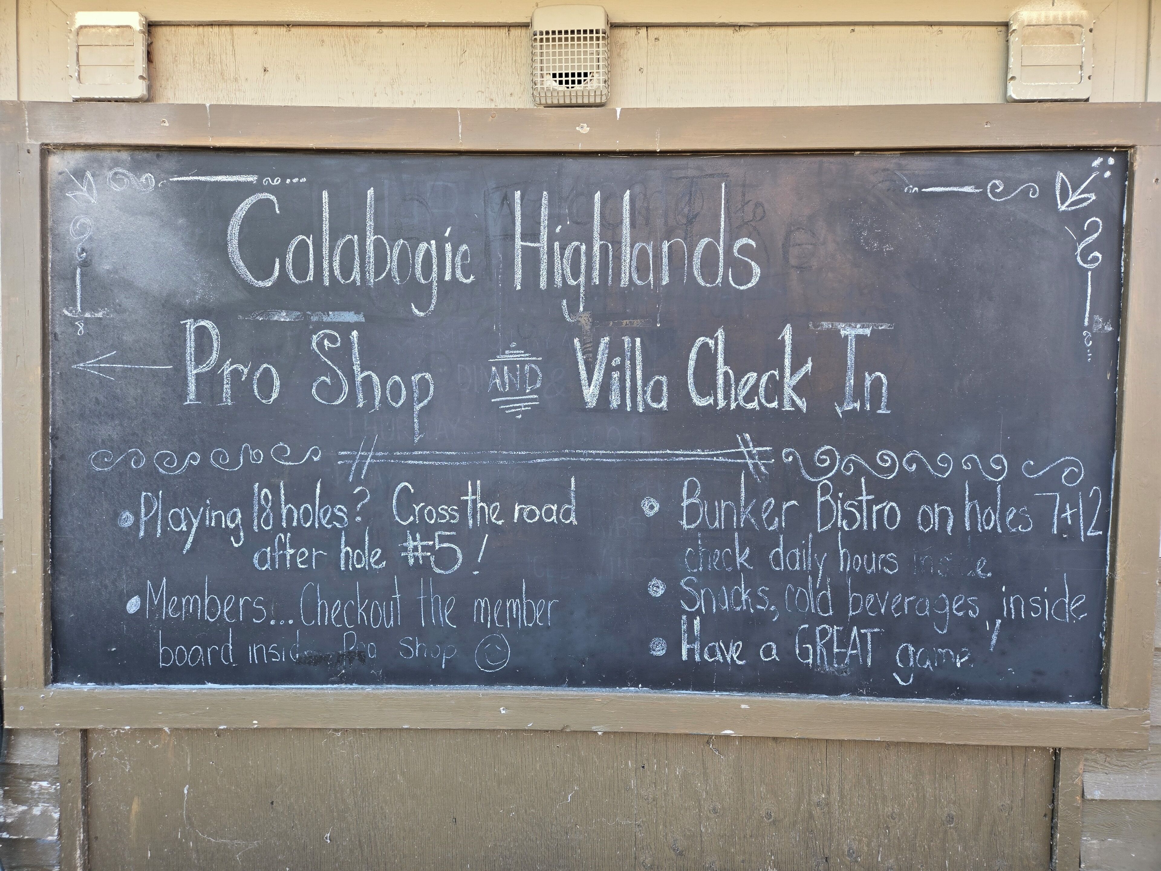 A chalkboard sign advertising 'Colabogie Highlands Pro Shop' and 'Villa Check In' with details about playing 18 holes, a bunker bistro, and member checkout.