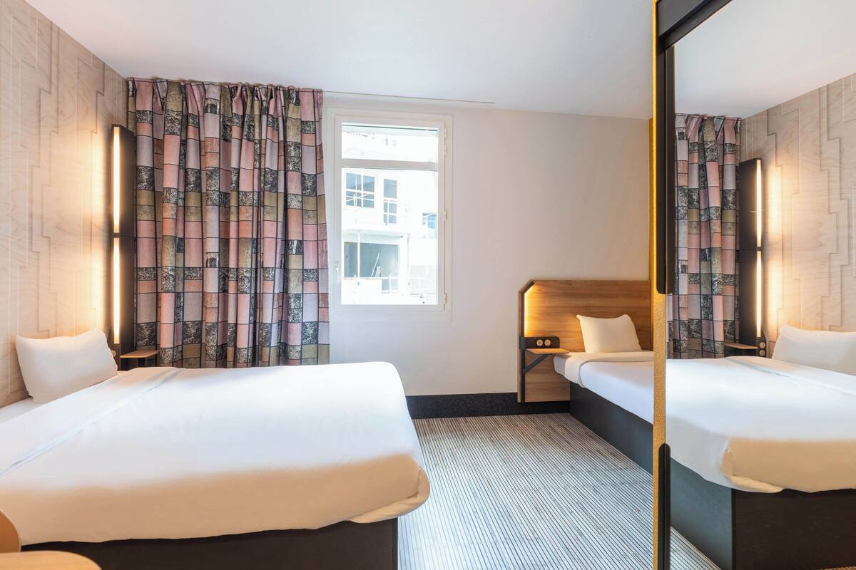 A hotel room with two beds, a large mirror, and a window with curtains.