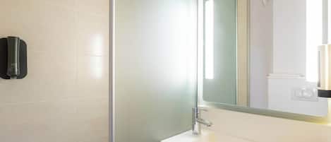 A modern bathroom with a white sink, a mirror, and a glass shower enclosure.