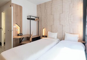 Een hotelkamer met twee bedden, een bureau, een stoel, een kapstok en een muur met een geometrisch patroon.