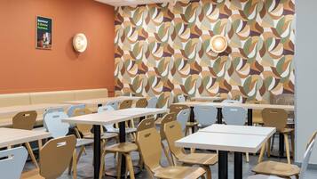 Una cafetería con varias mesas y sillas, un papel tapiz estampado y un cartel en la pared.
