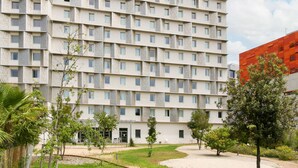 Un hotel de varios pisos con fachada moderna, numerosas ventanas y un patio ajardinado con árboles y un sendero.