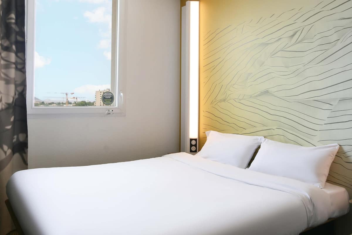 Una habitación de hotel con cama, ventana, un reloj de pared y vistas al exterior.