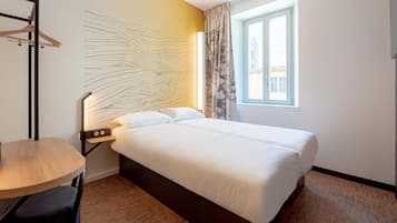 Habitación de hotel con cama, escritorio, silla, cuadro en la pared, ventana con cortinas y vistas al exterior.
