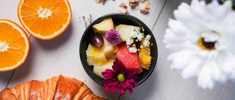 A breakfast setting with a bowl of fruit, a croissant, and a glass of coffee.