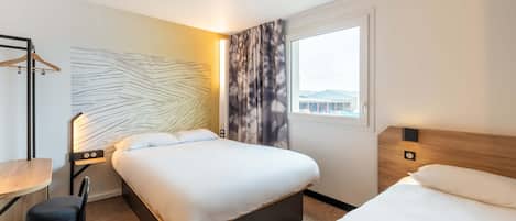 A hotel room with a large bed, a bedside table, a chair, a wall art piece, and a window with a view.