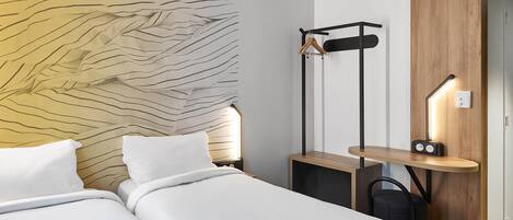 A modern hotel room with two beds, a wooden headboard, a wooden side table with a radio, and a coat rack.