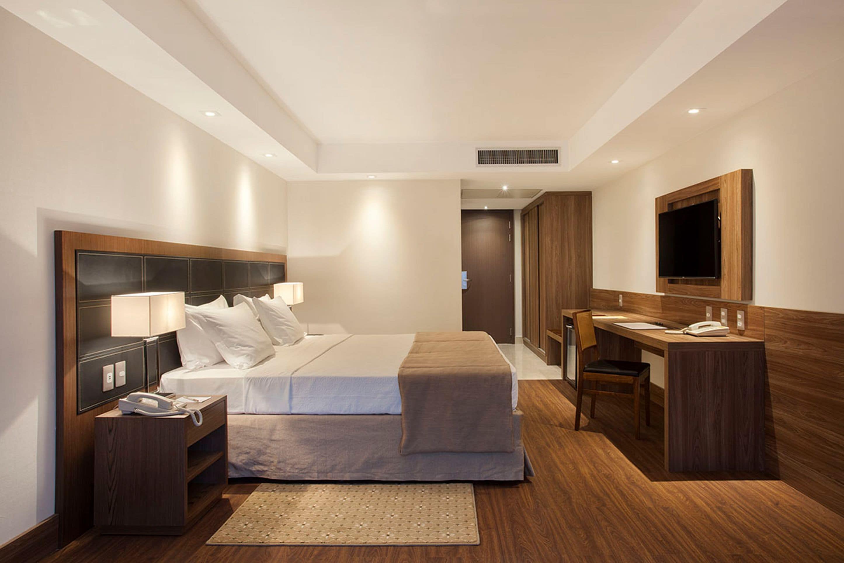 A modern hotel room with a large bed, bedside tables, a desk, and a mirror.