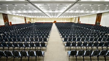 Un'ampia sala conferenze ben illuminata, con file di sedie nere e pavimento rivestito a moquette.