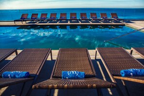 A poolside area with lounge chairs and a view of the ocean.