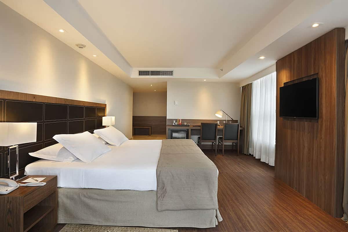 Habitación de hotel con una cama grande, un escritorio, un televisor y un baño visible a través de una puerta abierta.