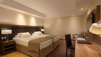 Quarto de hotel com duas camas, uma mesa, uma cadeira, uma televisão e um abajur.