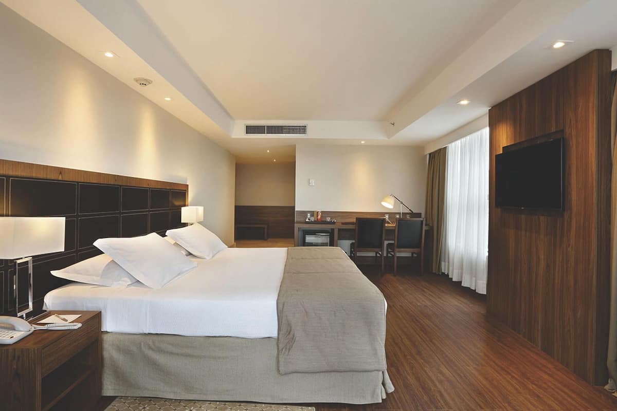 Una habitación de hotel con una cama grande, mesitas de noche, un escritorio, una silla, un televisor y una ventana con cortinas.