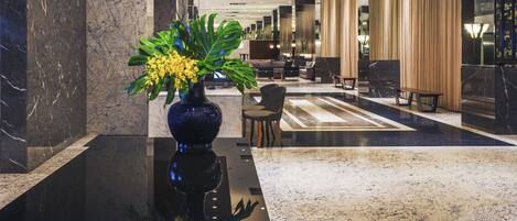 A modern lobby with marble flooring, a large vase with flowers, and a seating area with chairs and a sofa.