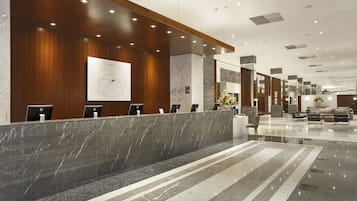 A modern hotel lobby with a reception desk, seating area, and a large clock on the wall.
