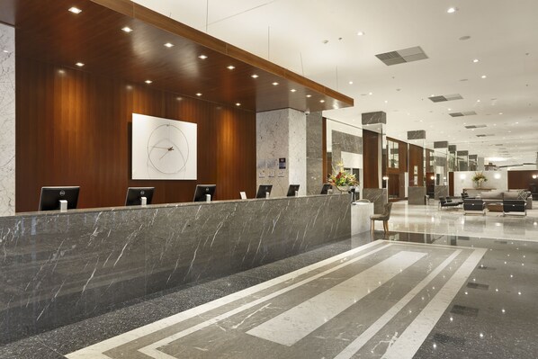 A modern hotel lobby with a reception desk, seating area, and a large clock on the wall.