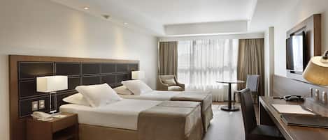 A hotel room with two beds, a desk, a chair, a TV, and a window with curtains.