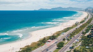 A coastal road with a beach on one side and a cityscape on the other. - Windsor Oceanico (Rio de Janeiro)