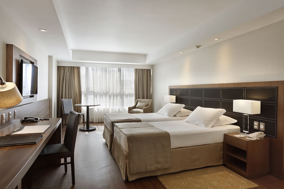 Habitación de hotel con dos camas, un escritorio, una silla, un televisor y una lámpara.