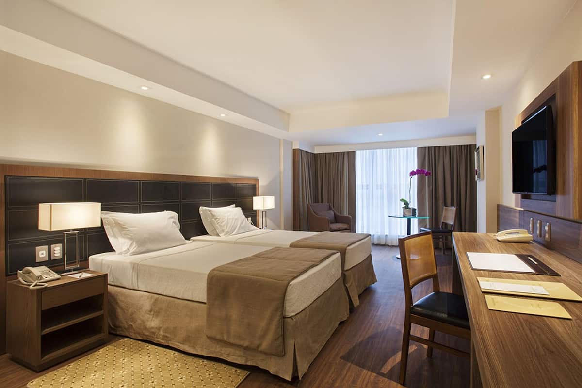 Habitación de hotel con dos camas, un escritorio, una silla, un televisor y una ventana con cortinas.