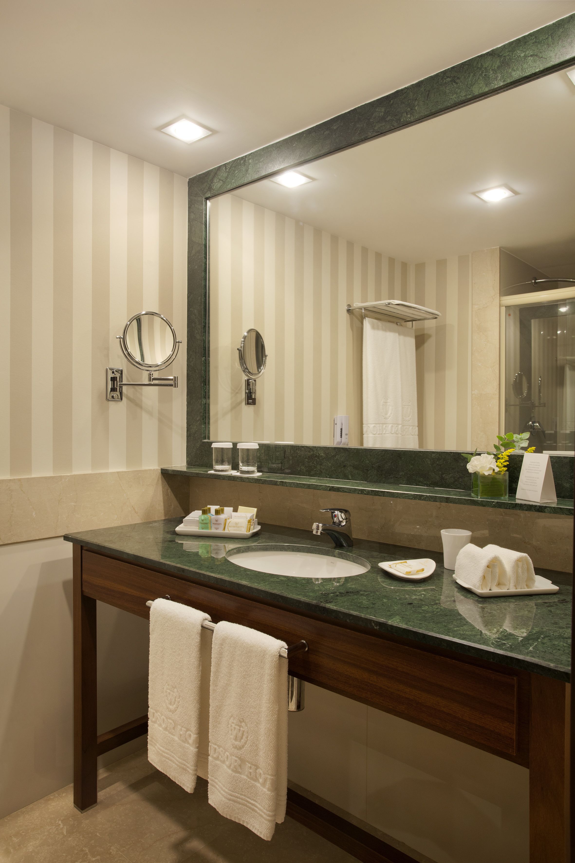 A modern bathroom with a marble sink, a large mirror, and striped wallpaper.