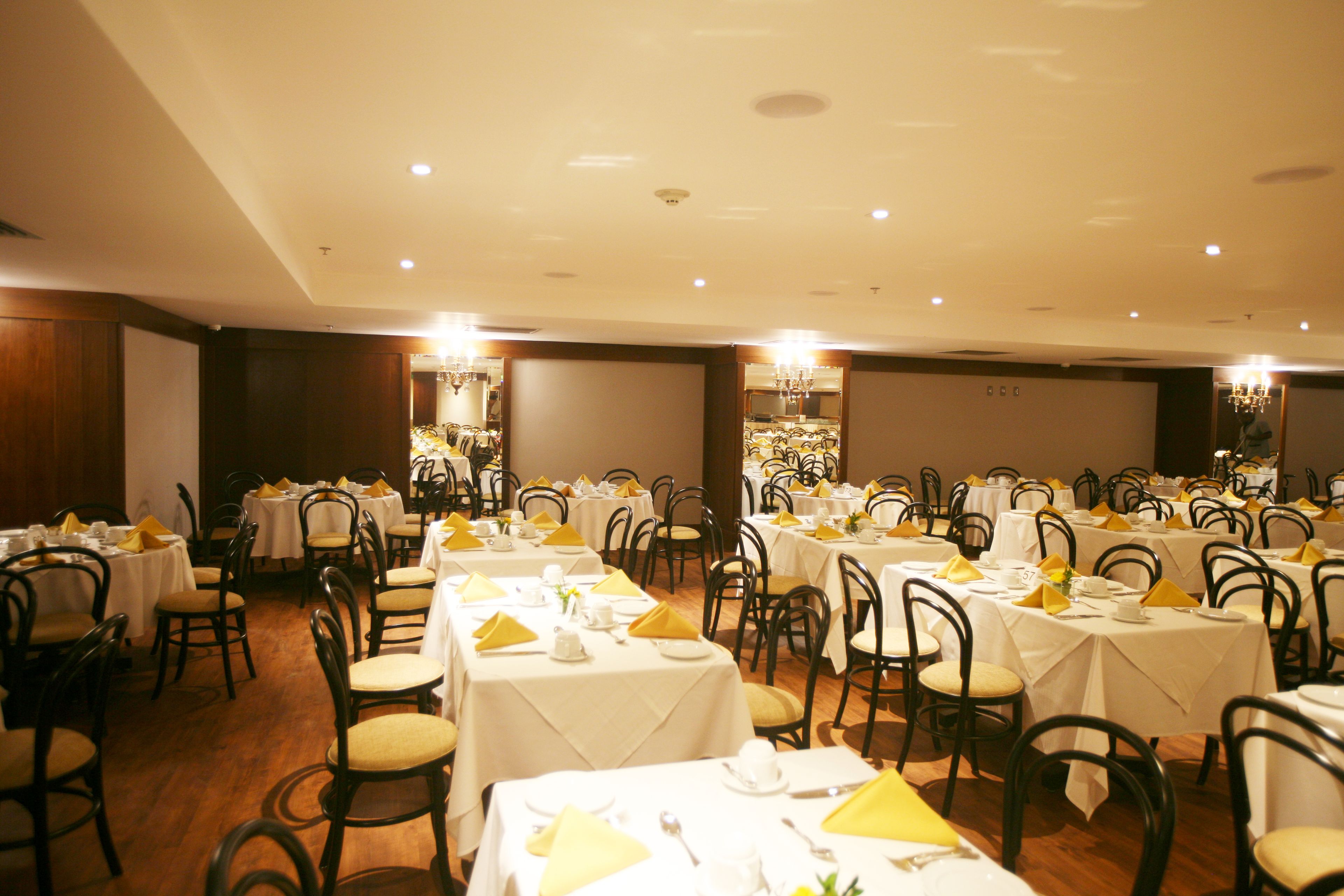 Une salle de banquet avec de nombreuses tables rondes, chacune recouverte d’une nappe blanche, agrémentée de serviettes jaunes et de couverts en argent.