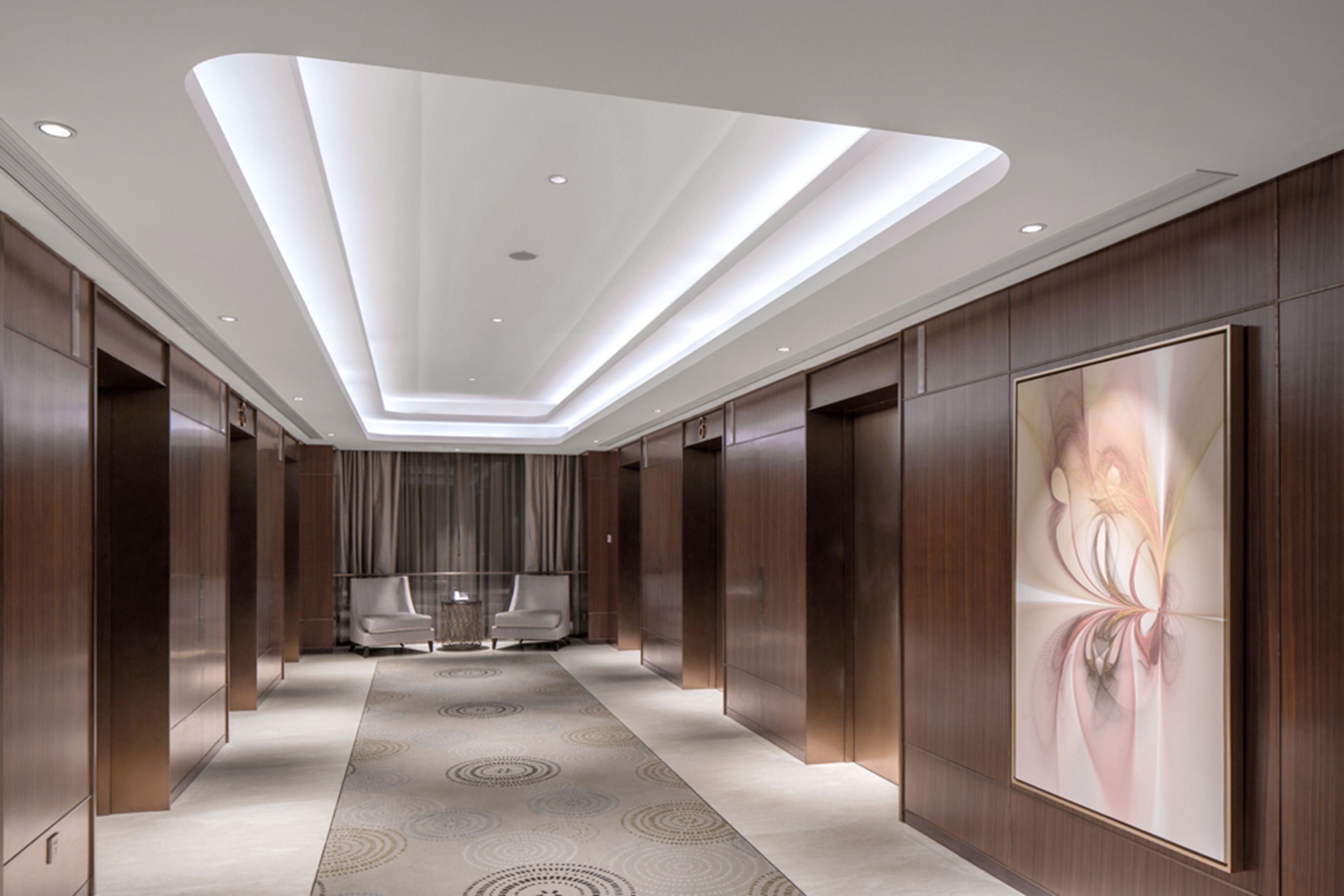 Passadís modern d'hotel amb zona d'estar central, il·luminació empotrada i una gran obra d'art a la paret.