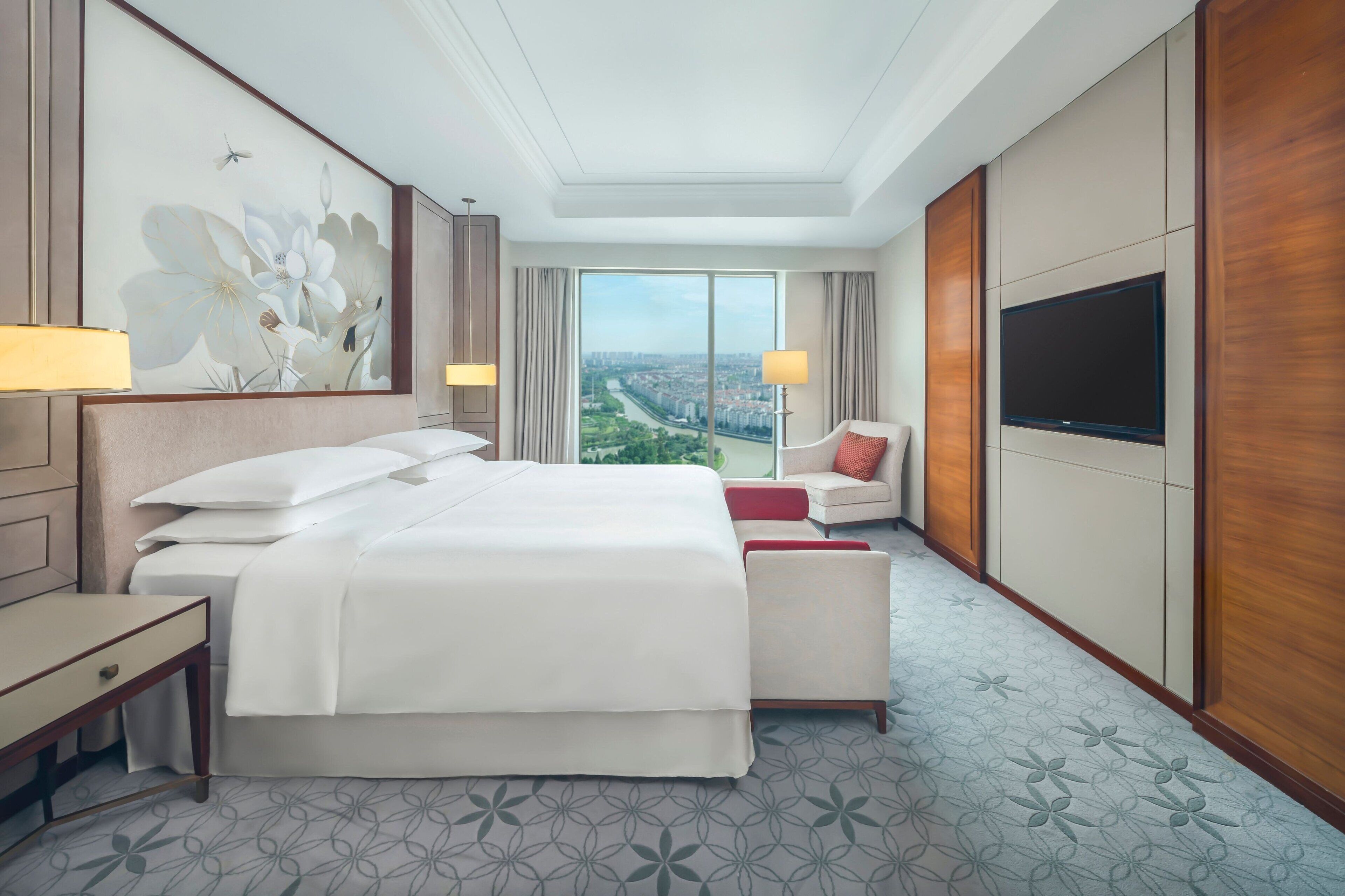 Habitación de hotel con una cama grande, un escritorio, un televisor y vistas a un paisaje urbano.