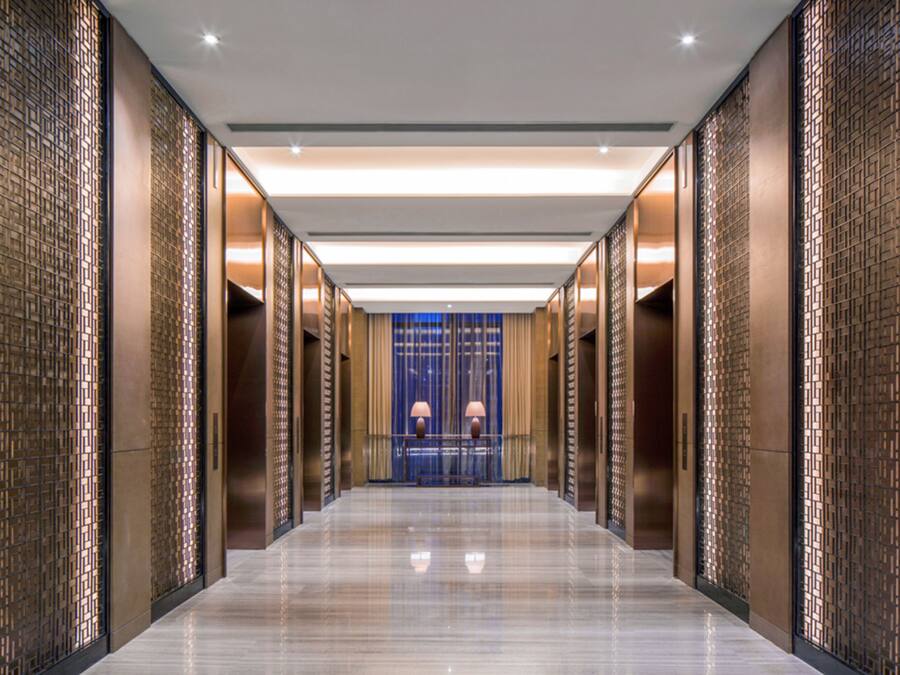 A modern hotel corridor with a reflective floor, decorative panels, and a blue door at the end.