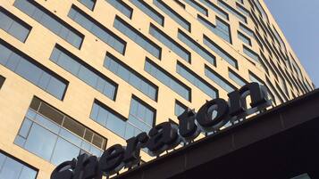 A high-rise hotel building with a modern architectural design, featuring a prominent 'Sheraton' sign at the top.