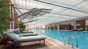 An indoor swimming pool with lounge chairs and umbrellas. - Sheraton Shanghai Jiading Hotel (Shanghai)