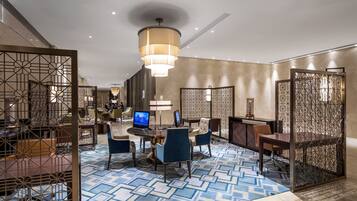 Um saguão moderno de hotel com uma mesa redonda, cadeiras azuis, um lustre grande e painéis decorativos.