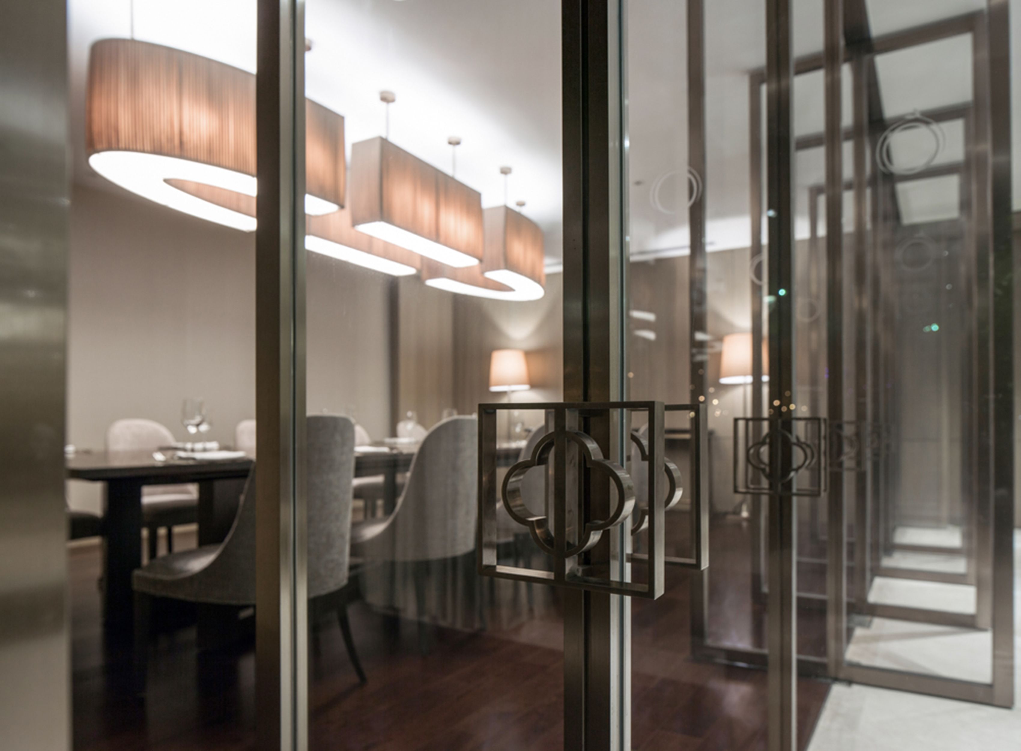 A modern interior with a dining area, glass partitions, and contemporary lighting fixtures.
