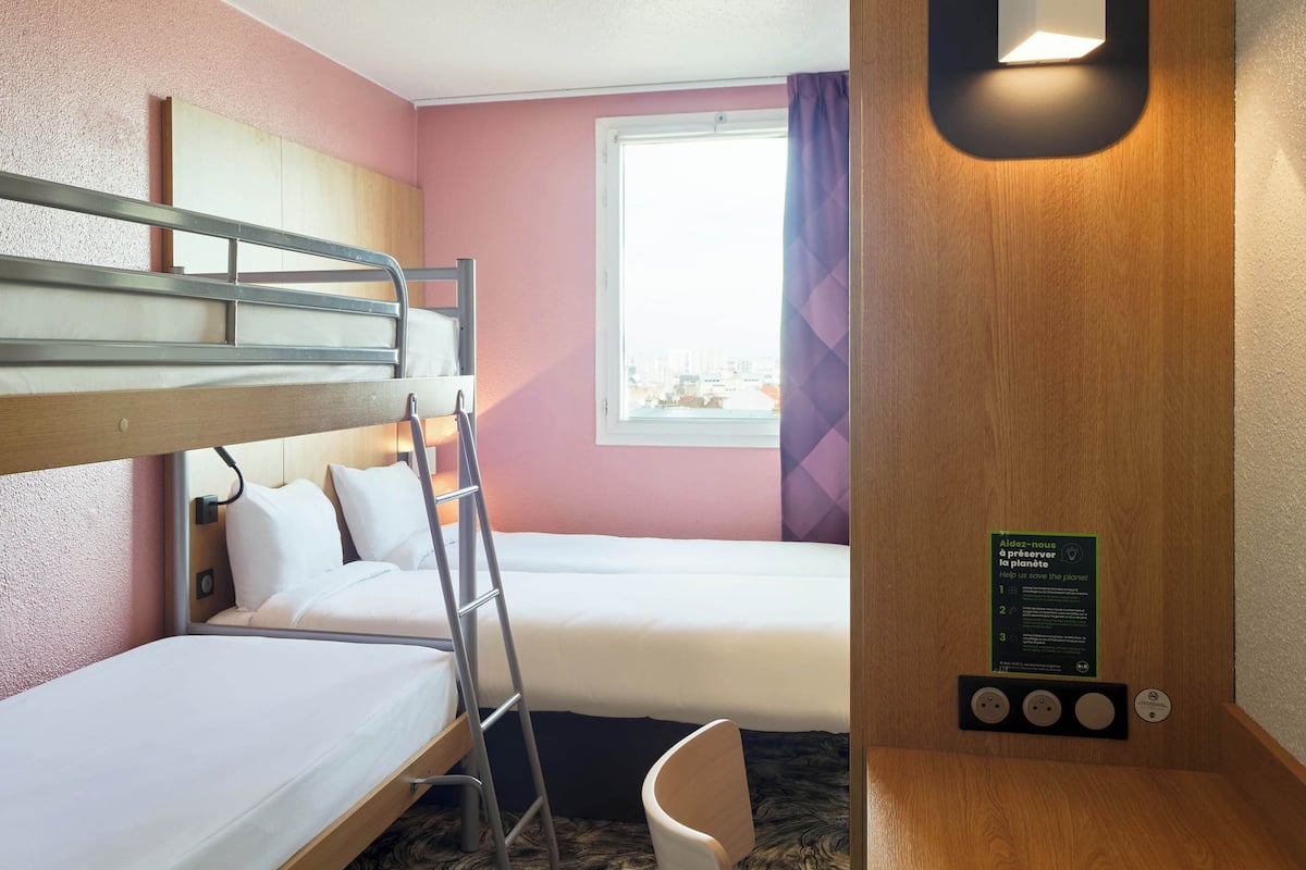 A hotel room with bunk beds, a window with curtains, a wooden desk, and a sign with environmental information.