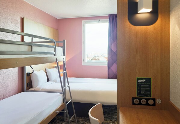 Une chambre d’hôtel avec des lits superposés, une fenêtre avec des rideaux, un bureau en bois et un panneau d’information sur l’environnement.