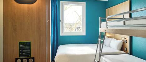A compact hotel room with two bunk beds, a window with curtains, a wooden wall with a light fixture, and a sign about environmental preservation.