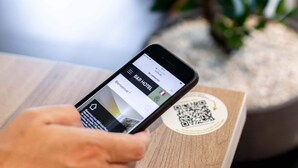 A smartphone displaying a hotel booking app with a QR code on a wooden surface. - B&B HOTEL Paris Porte de la Villette (Aubervilliers)