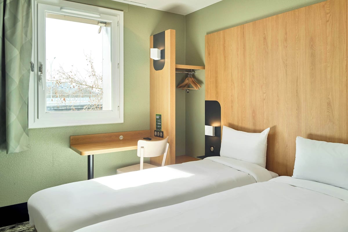 A hotel room with a bed, a desk, a chair, a wardrobe, and a window.