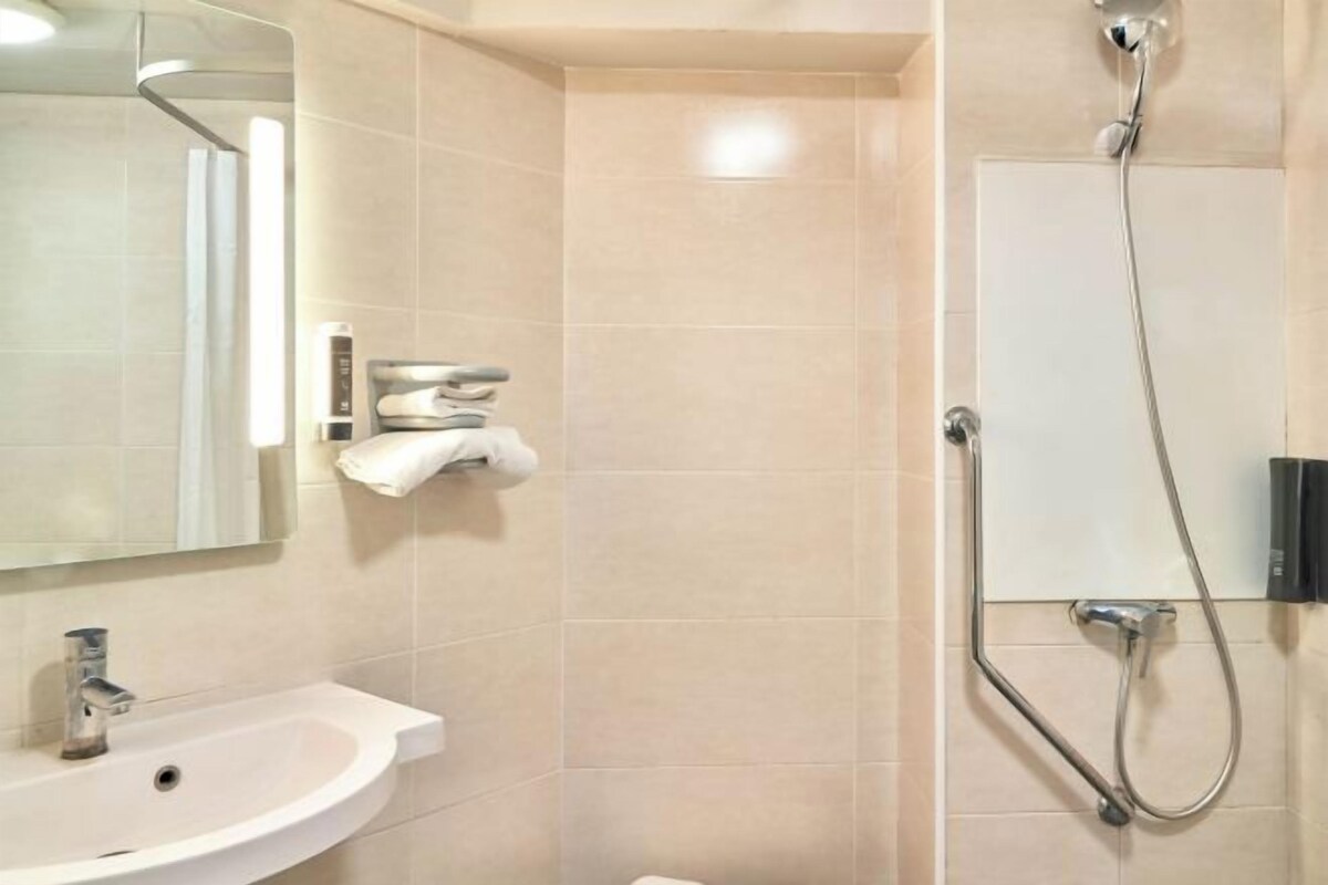 Un baño con lavamanos, espejo, toallero y ducha.