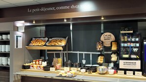 A breakfast buffet with various food items and a sign that reads "Le petit-déjeuner, comme chez vous." - B&B HOTEL Paris Porte de la Villette (Aubervilliers)