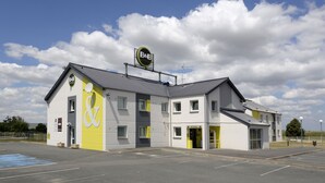 A B&B hotel with a yellow and white facade, a parking lot, and a clear sky.