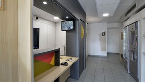 A modern, well-lit lobby with a reception desk, a mounted TV, and a refrigerator.