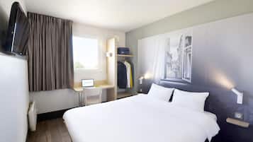 Habitació d'hotel amb un llit, un escriptori amb un ordinador, una televisió, una perxa de roba i una finestra amb cortines.