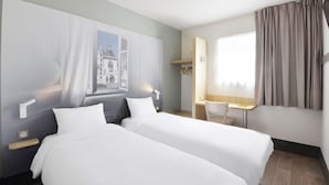 A hotel room with two beds, a desk, and a chair.