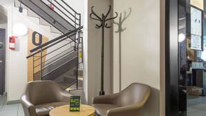 A lobby with two leather chairs, a small round table, a coat rack, and a staircase.