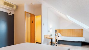 A hotel room with a bed, a desk, a chair, a wooden headboard, and a ceiling fan.