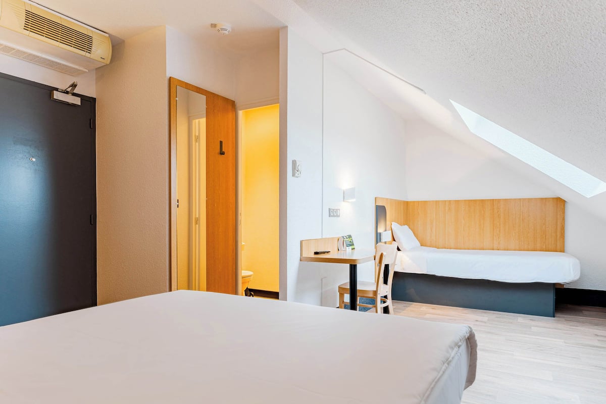 Habitación de hotel con cama, escritorio, silla, cabecera de madera y ventilador de techo.